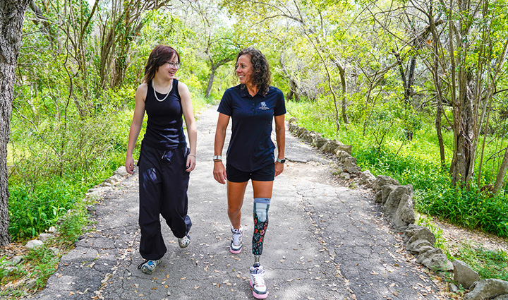 Wounded warrior Kelly Elmlinger with a prosthetic leg walking on a path though trees talking and laughing with her daughter.
