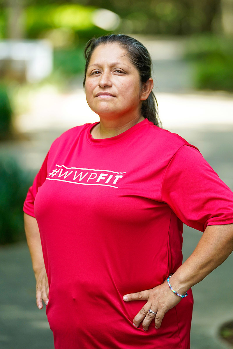 Wounded warrior Maria Edwards stands in a triumphant pose on a pathway. Her hands on her hips and her hair in a ponytail, she wears a slight smile for the camera.