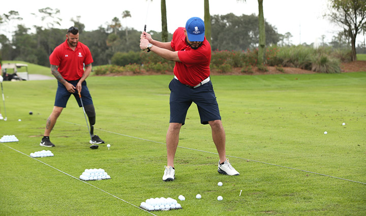 Two warriors in red WWP polos practice at the driving range during a golf fundraiser supporting Wounded Warrior Project.