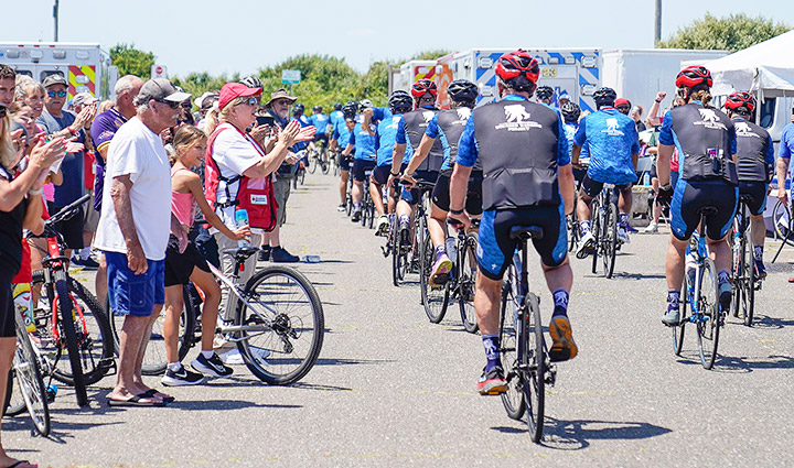 A group of supporters stands on the sidelines, cheering for the wounded warriors as they ride together on various bikes, wearing WWP riding gear.