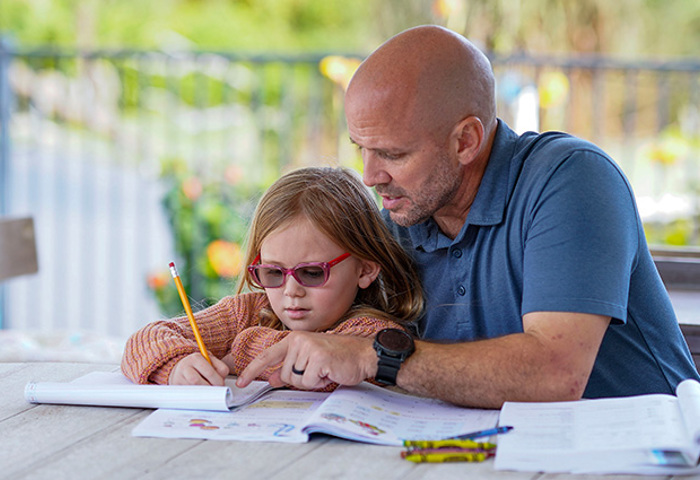 Warrior Dan Nevins sits with a child, working together on an activity and focusing on the open workbook in front of them.