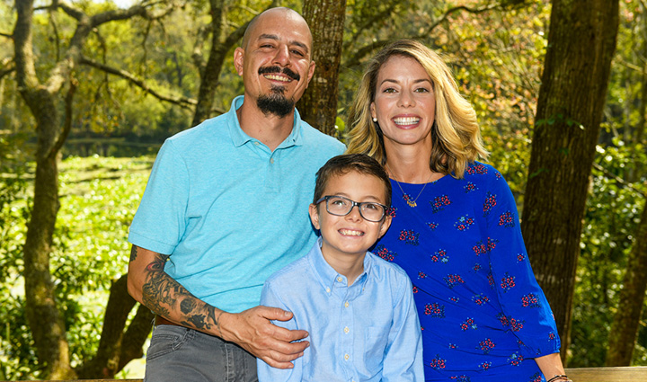 Warrior Felix Santiago poses with his wife and son outside, all smiling and wearing different shades of blue.