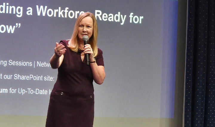 During a speech, family support member Jennifer Jenkins wears a maroon dress while gesturing toward the audience.
