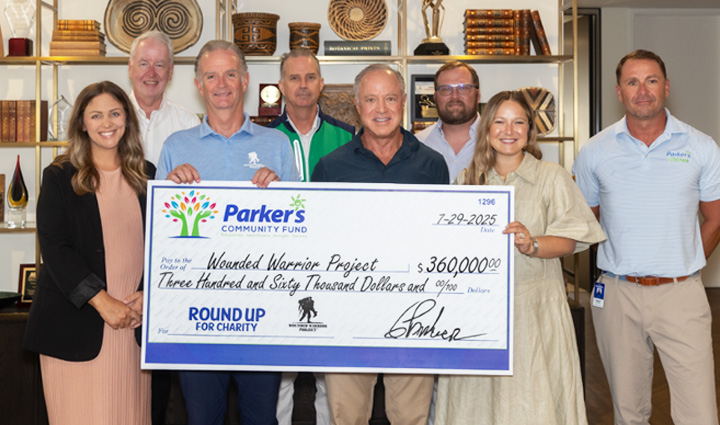 WWP CEO Walt Piatt and Parker’s Kitchen executive Greg Parker stand holding a large donation check surrounded by both male and female staff.