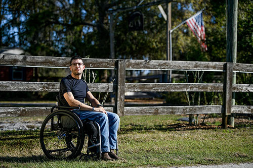 Veteran Mark Lalli sitting in a wheelchair in a field in front of a U.S. flag.