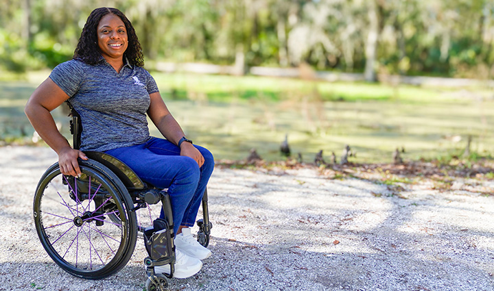 Wounded warrior Corine Hamilton sits outside in her wheelchair while smiling at the camera.